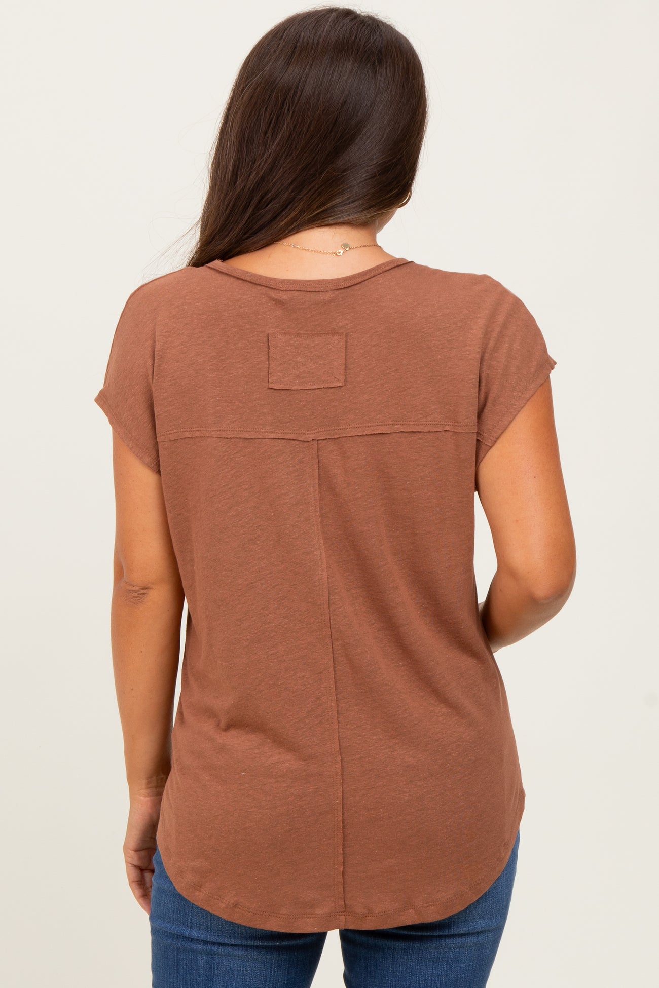 woman wearing a brown maternity top with short sleeves and a curved hem, viewed from the back