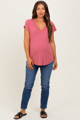 woman wearing a dusty rose v-neck maternity top and blue skinny jeans, showing her baby bump
