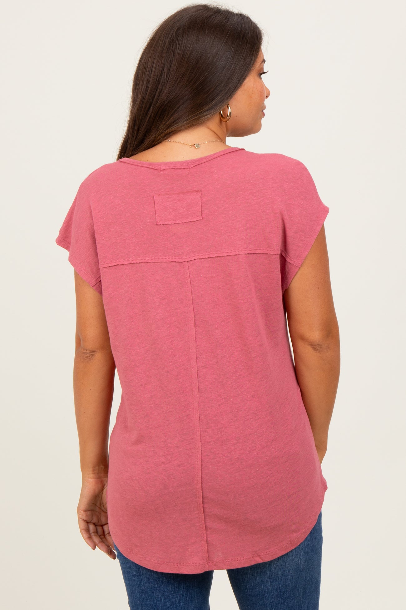woman wearing a pink maternity top with short sleeves and a relaxed fit, standing with her back to the camera