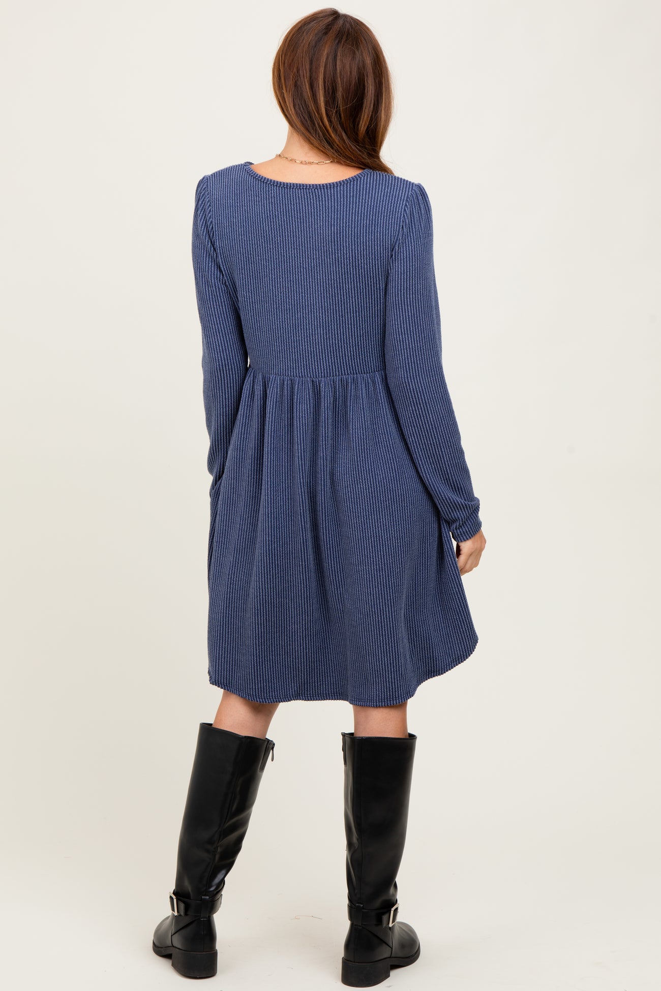 woman wearing a navy blue striped long sleeve dress with a flared skirt and black knee-high boots, seen from the back
