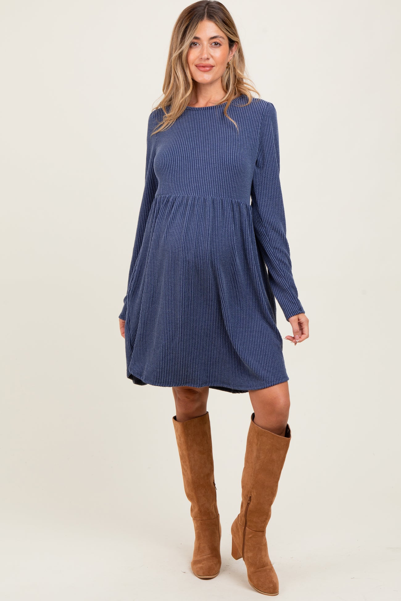 woman wearing a navy striped long sleeve maternity dress with a flowing skirt and knee-high brown boots, showing a baby bump