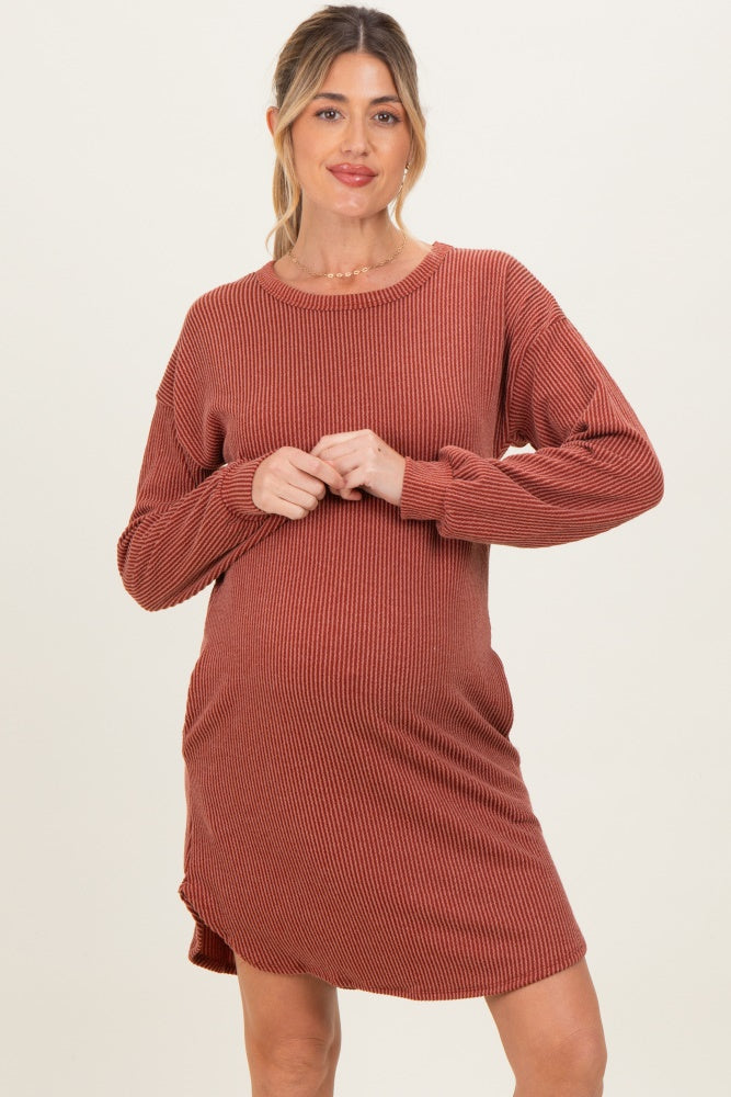 woman wearing a rust ribbed maternity dress with long sleeves and a curved hem, showcasing her baby bump