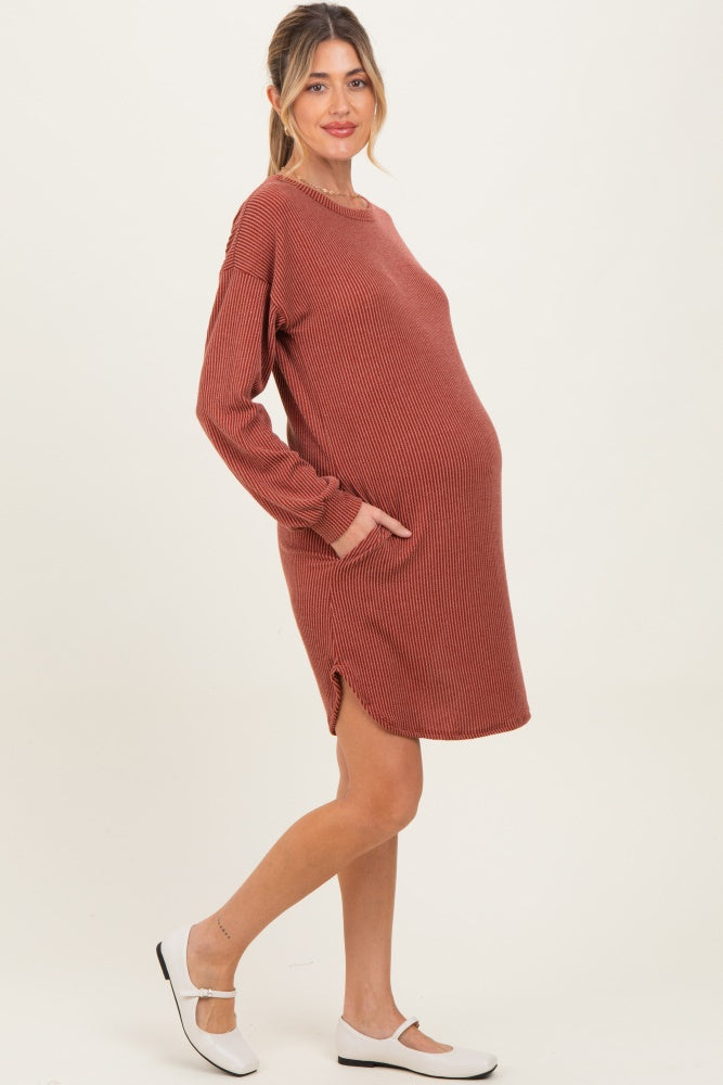 woman wearing a rust colored ribbed maternity dress with long sleeves and pockets, showing her baby bump