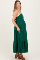 woman wearing a green tiered maternity maxi dress with spaghetti straps and a visible baby bump