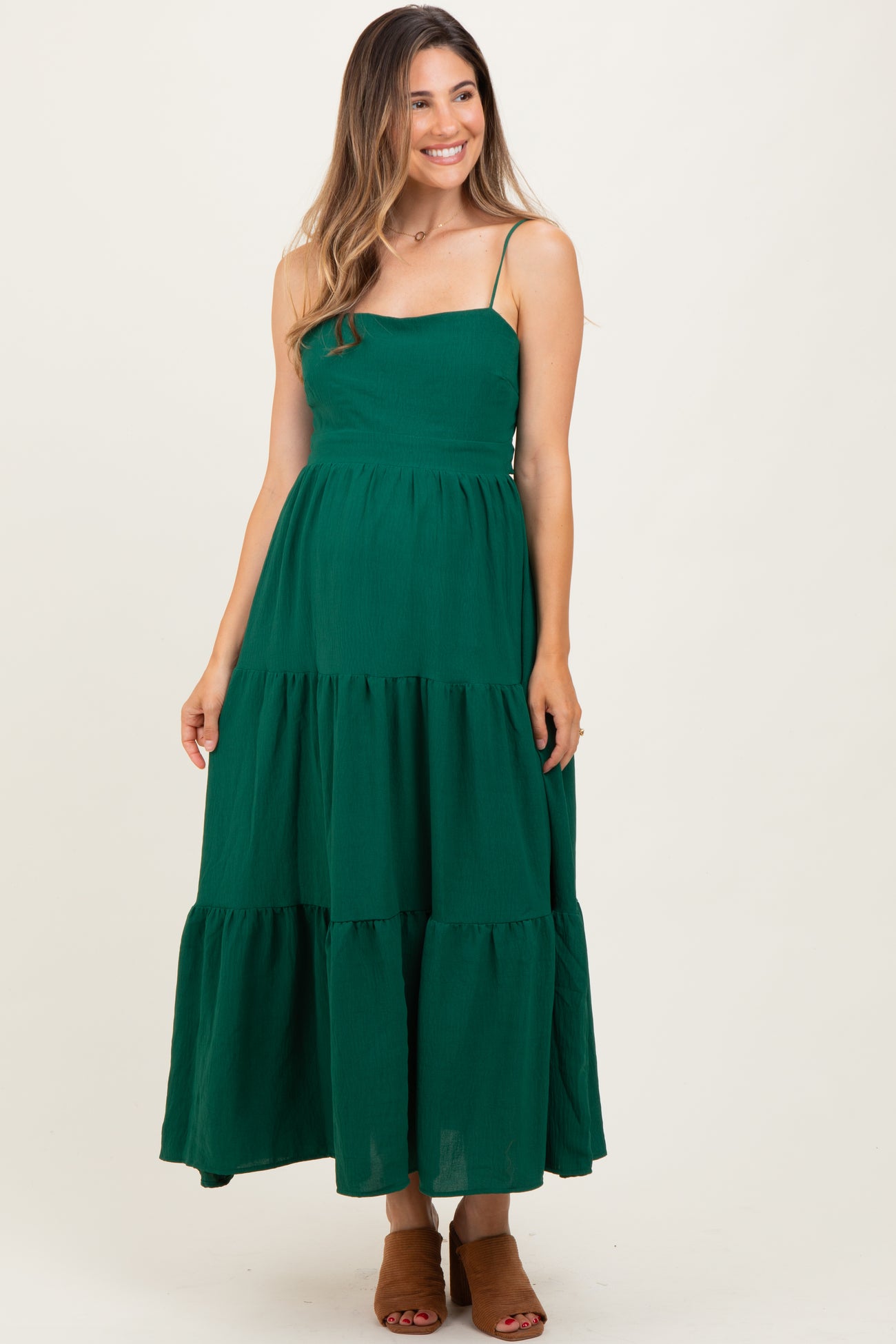 woman wearing a green maternity maxi dress with adjustable spaghetti straps and tiered ruffle details