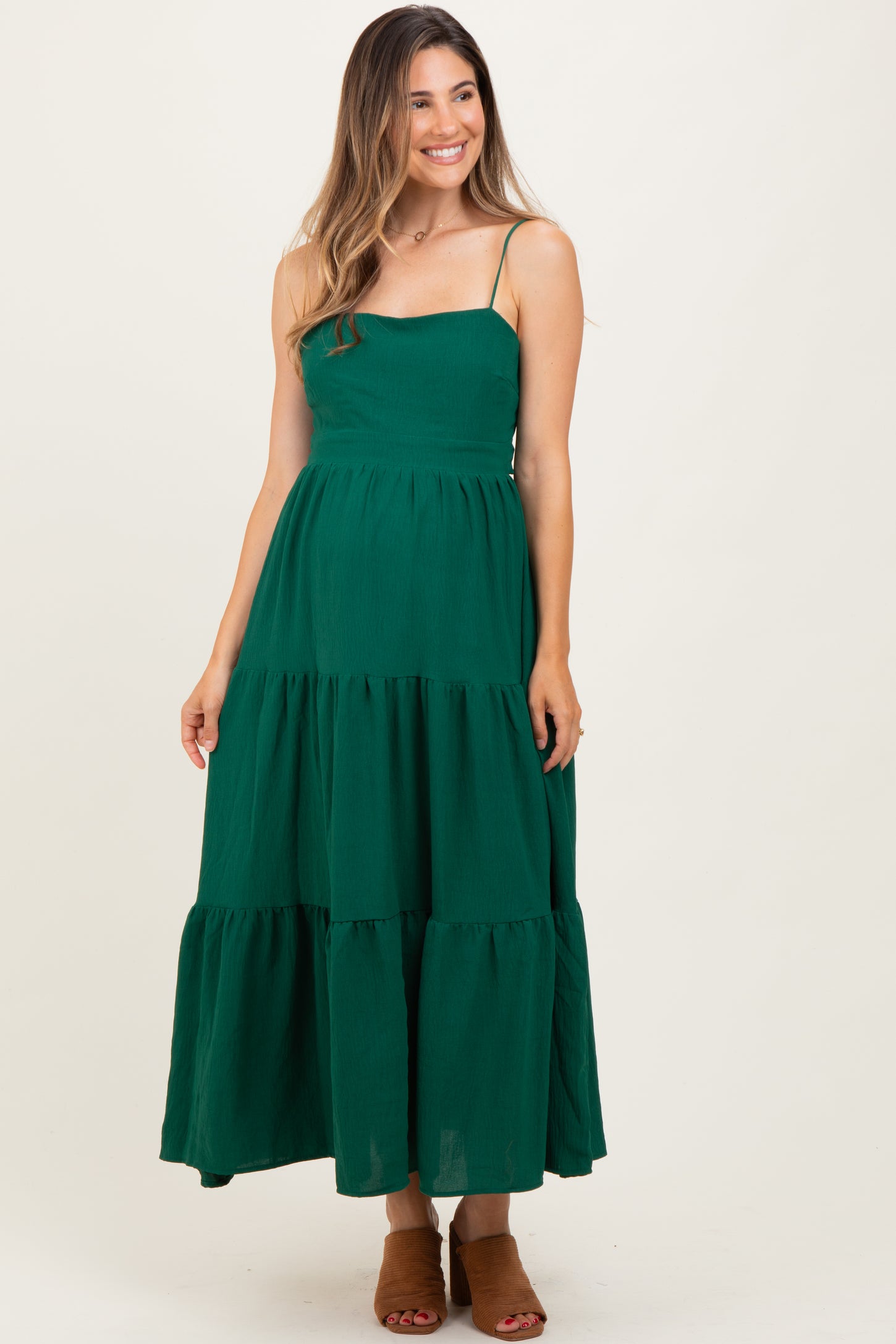 woman wearing a green maternity maxi dress with adjustable spaghetti straps and tiered ruffle details