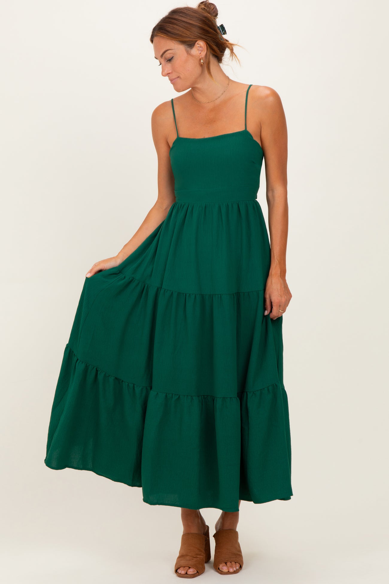 woman wearing a dark green tiered maxi dress with spaghetti straps and a fitted bodice, holding the skirt gently