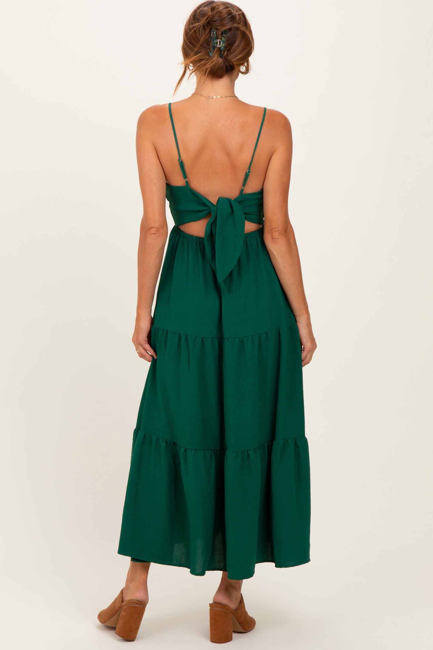 woman wearing a dark green tiered maxi dress with a tied back detail and open back design