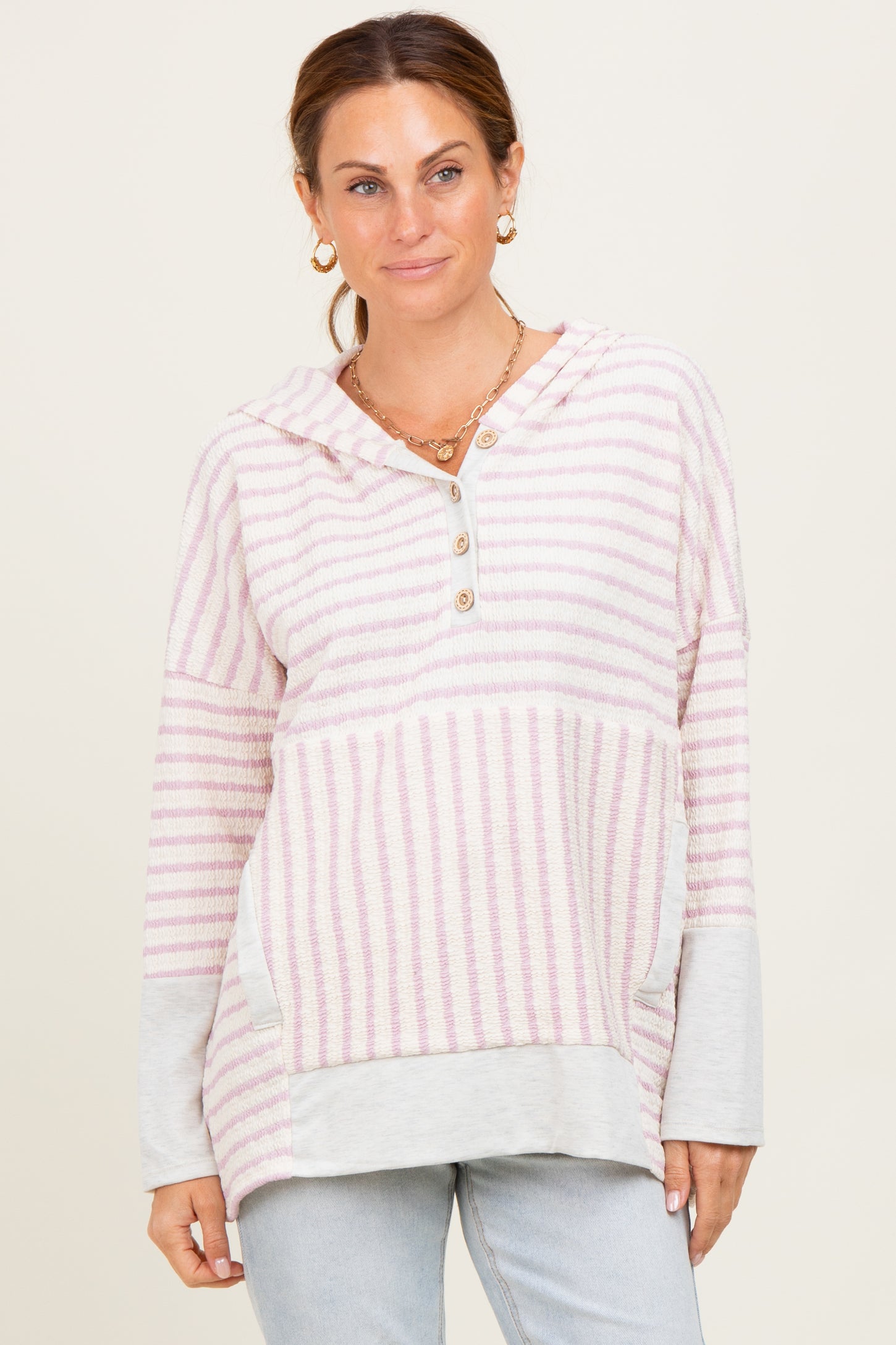 woman wearing a pink and white striped hooded pullover with a button detail and gray sleeves