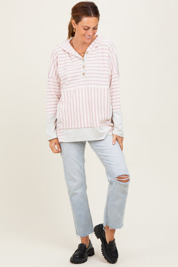 woman wearing a pink and white striped pullover hoodie with a button detail, paired with ripped light blue jeans and black slip-on shoes