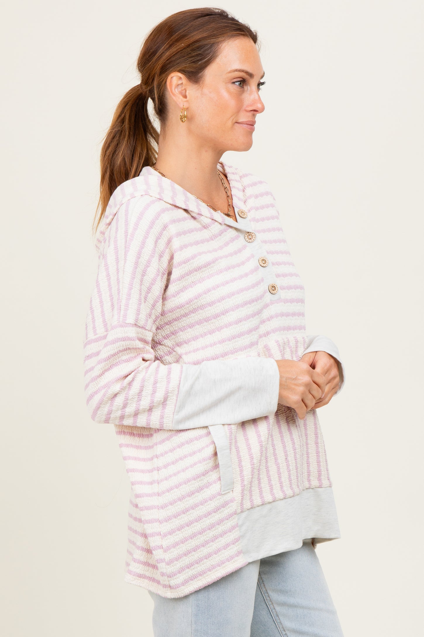 woman wearing a pink and white striped hooded sweater with button details and a contrasting gray bottom