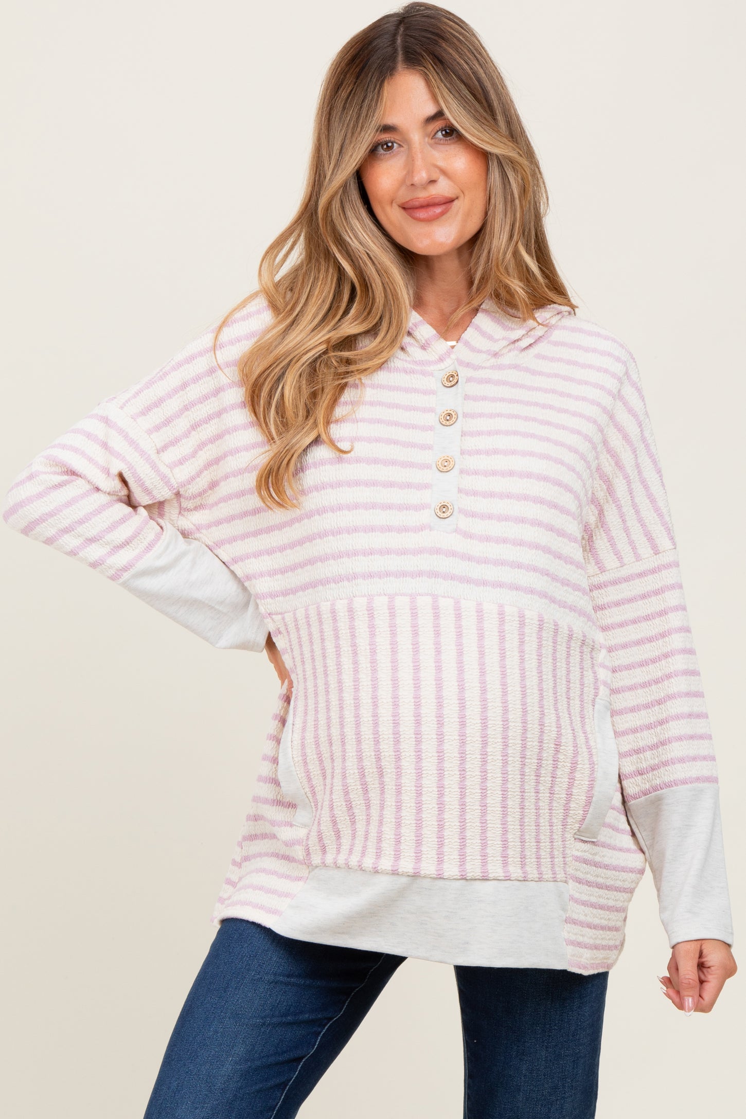 woman wearing a light pink and white striped maternity hoodie with buttons and a visible baby bump