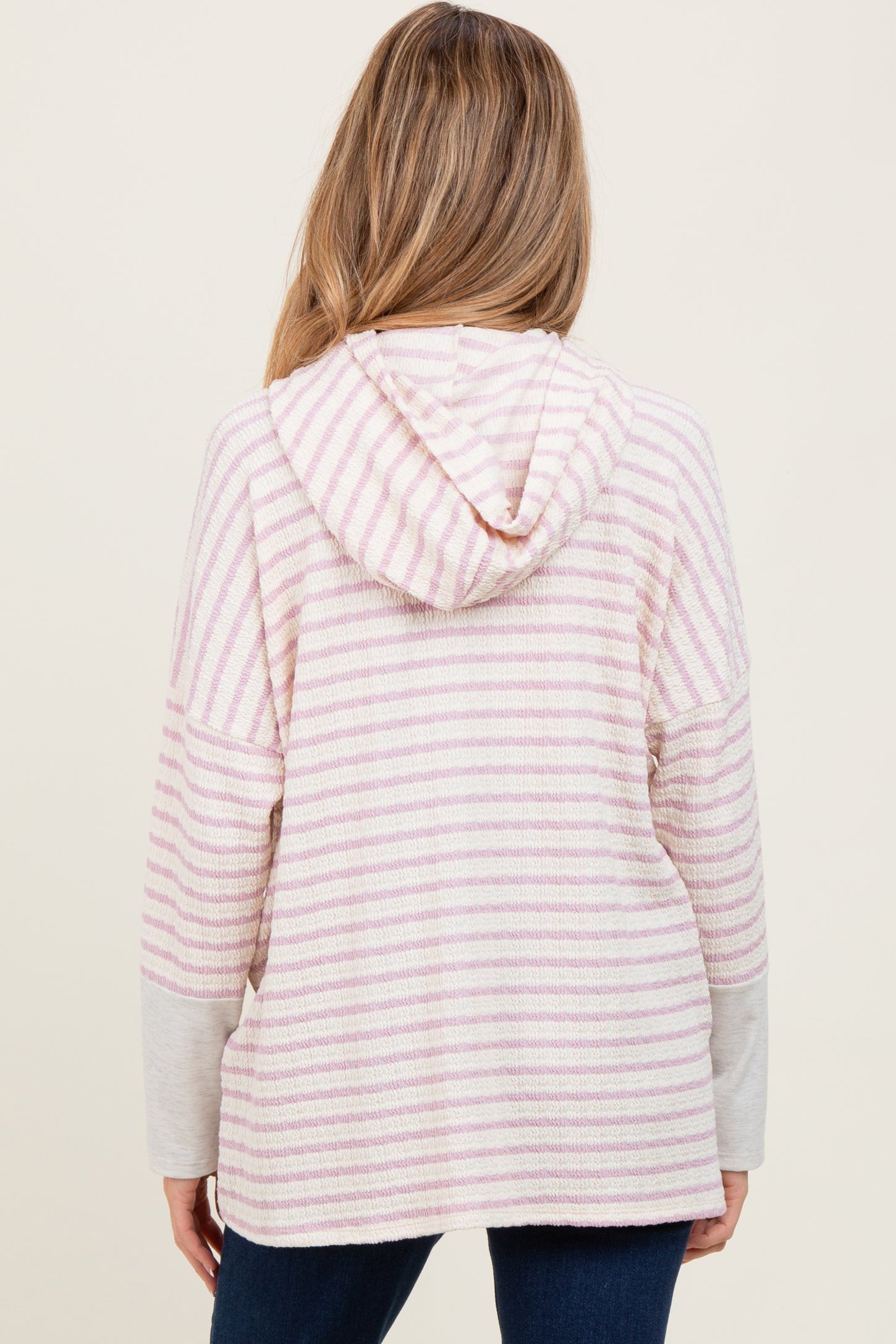 woman wearing a pink and white striped maternity hoodie with a hood and long sleeves, showing a relaxed fit from the back