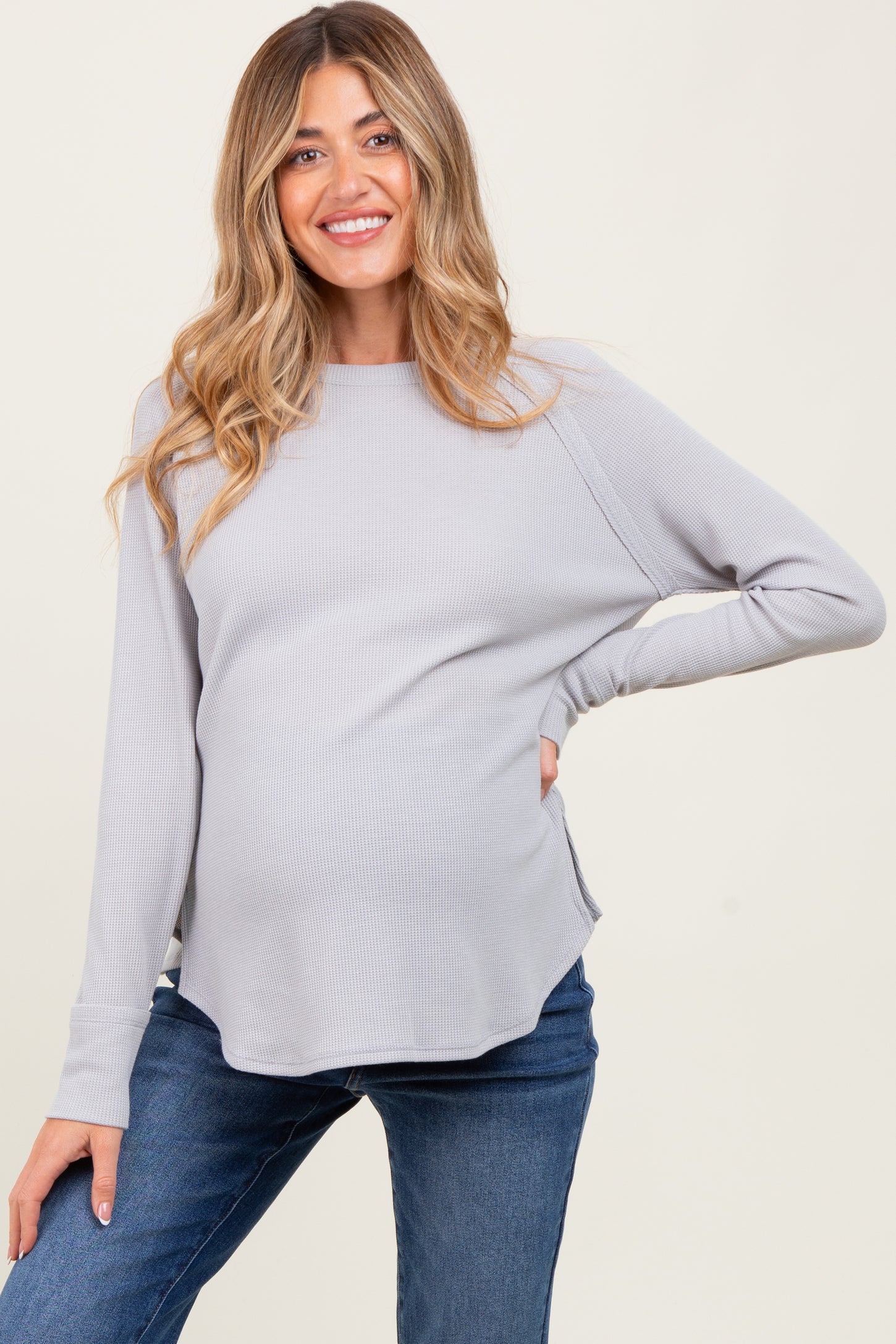 woman wearing a light gray ribbed maternity top with a curved hem and a visible baby bump