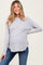 woman wearing a light gray ribbed maternity top with a curved hem and a visible baby bump