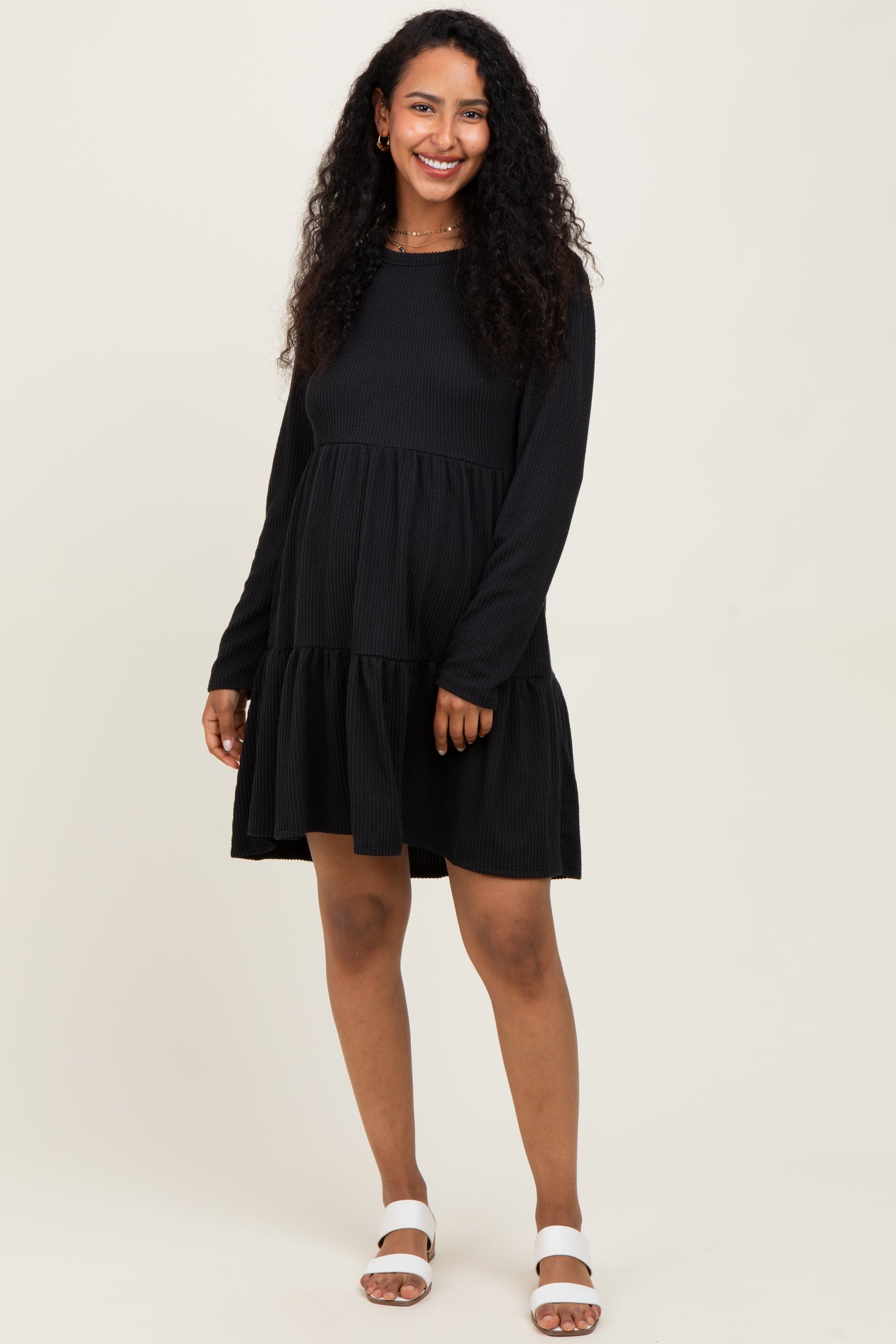 woman wearing a black long sleeve maternity dress with tiered ruffle hem and a visible baby bump