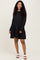 woman wearing a black long sleeve maternity dress with tiered ruffle hem and a visible baby bump
