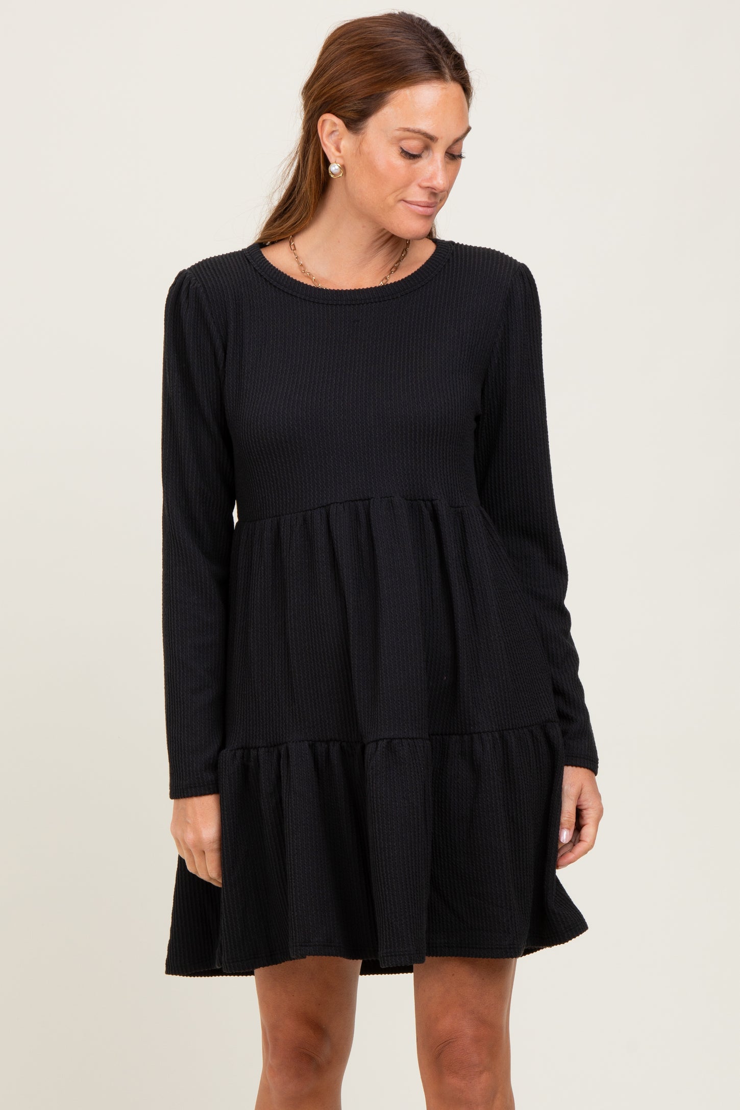 woman wearing a black long sleeve tiered dress with a textured fabric and round neckline