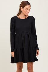 woman wearing a black long sleeve tiered dress with a textured fabric and round neckline