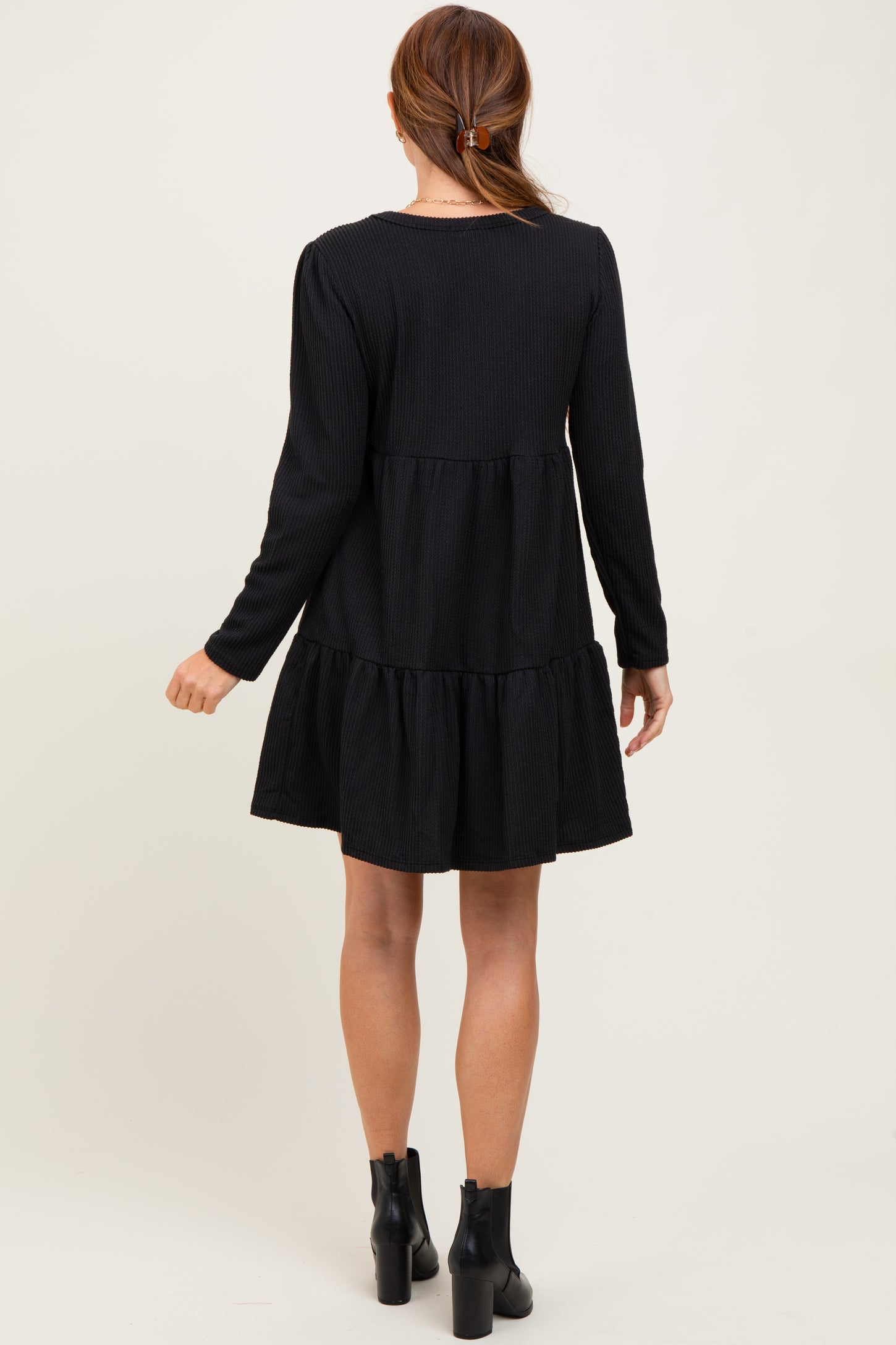 woman wearing a black long sleeve tiered dress with a flared skirt and ankle boots, seen from the back