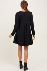 woman wearing a black long sleeve tiered dress with a flared skirt and ankle boots, seen from the back