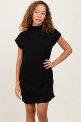 woman wearing a black short sleeve cowl neck dress, posing with one hand on her hip