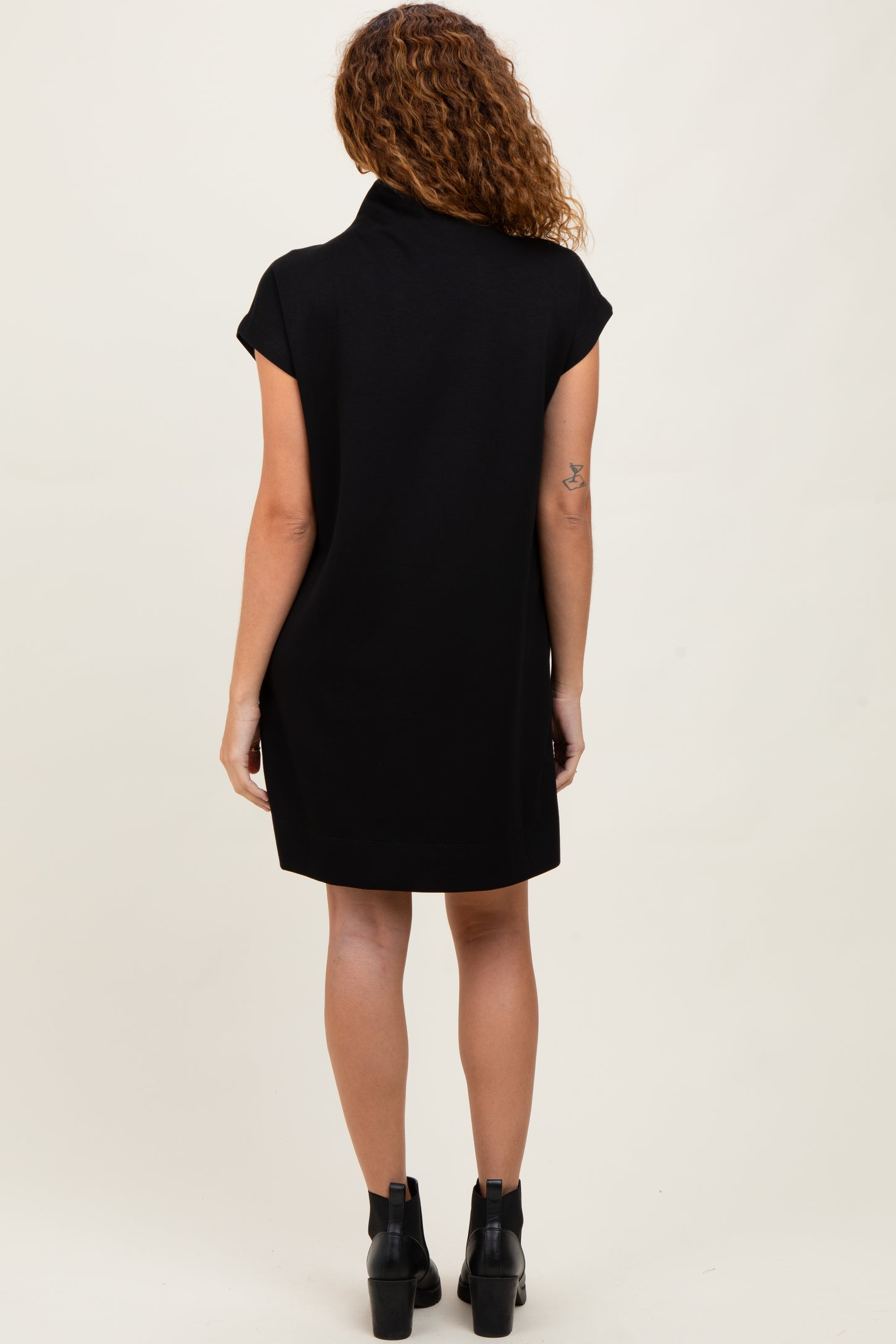 woman wearing a short-sleeve black dress with a high collar, standing with her back to the camera