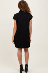 woman wearing a short-sleeve black dress with a high collar, standing with her back to the camera