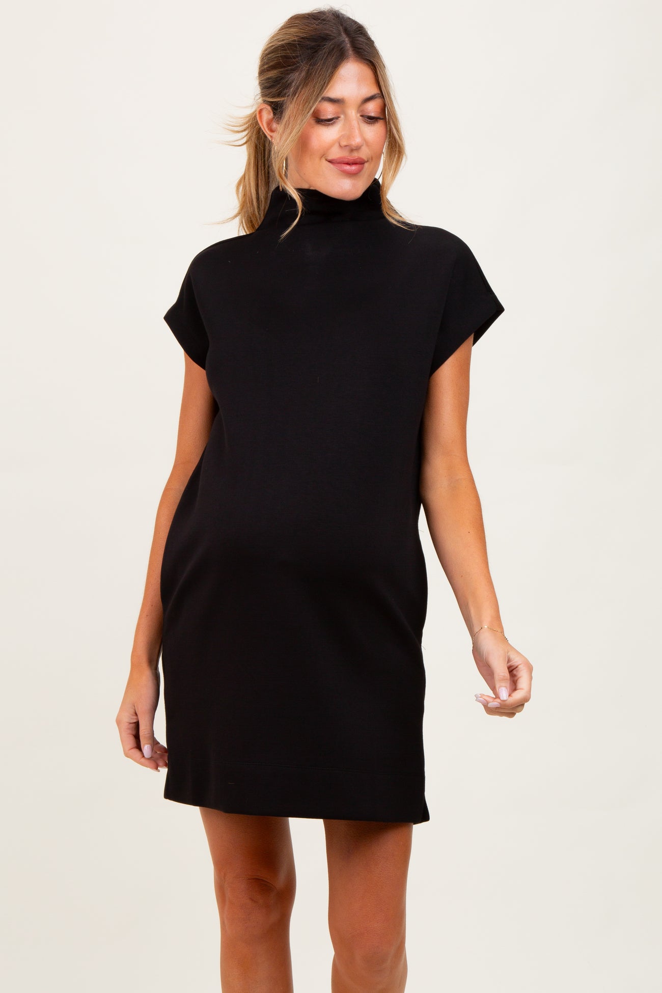 woman wearing a black maternity dress with a mock turtleneck and short sleeves, showing her baby bump