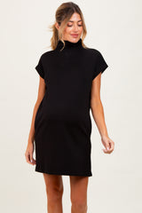 woman wearing a black maternity dress with a mock turtleneck and short sleeves, showing her baby bump