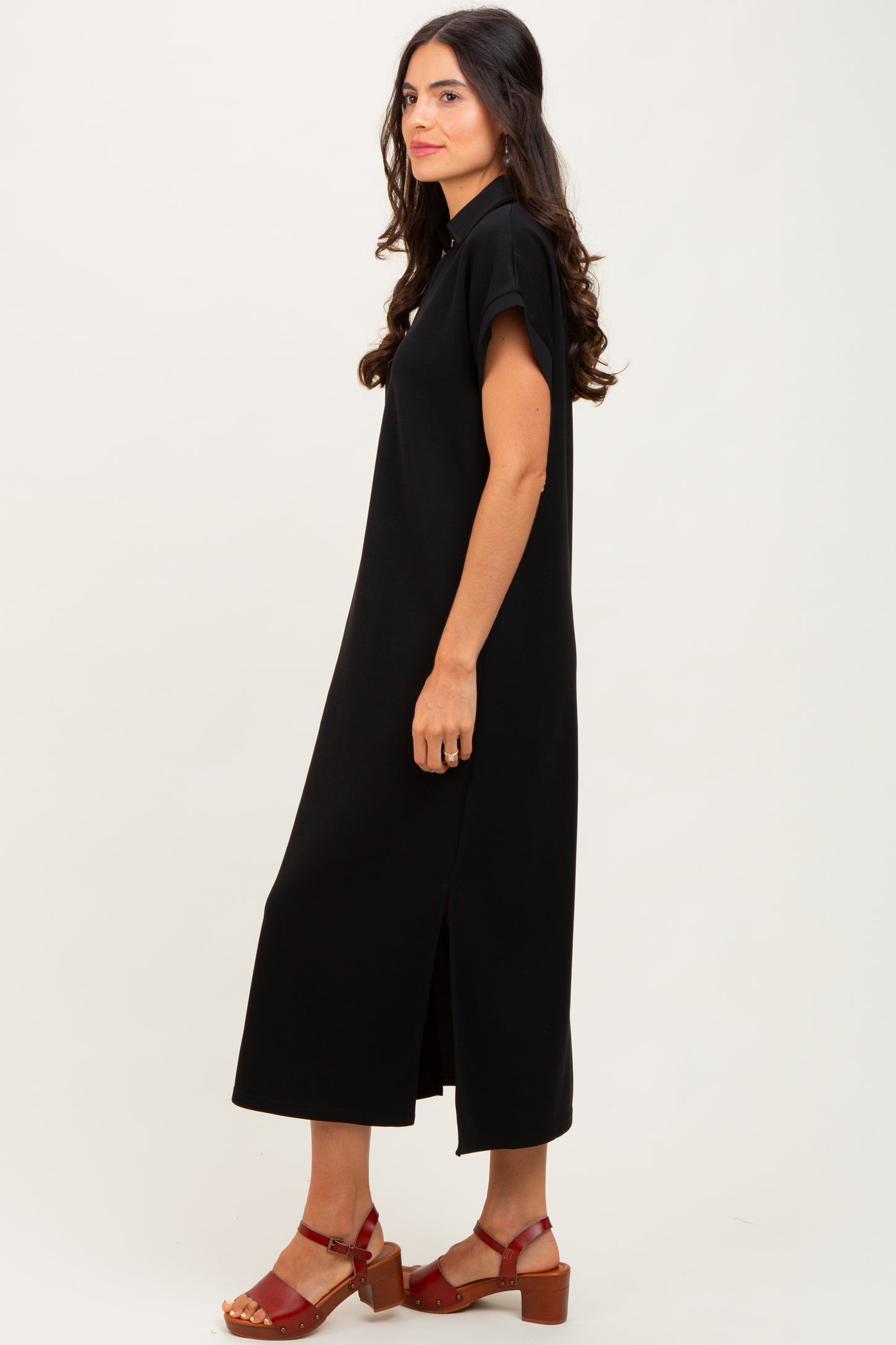 woman wearing a black midi dress with short sleeves and side slits, styled with red heeled sandals