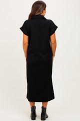 woman wearing a black short sleeve maternity dress, seen from the back, with a long silhouette and ankle boots