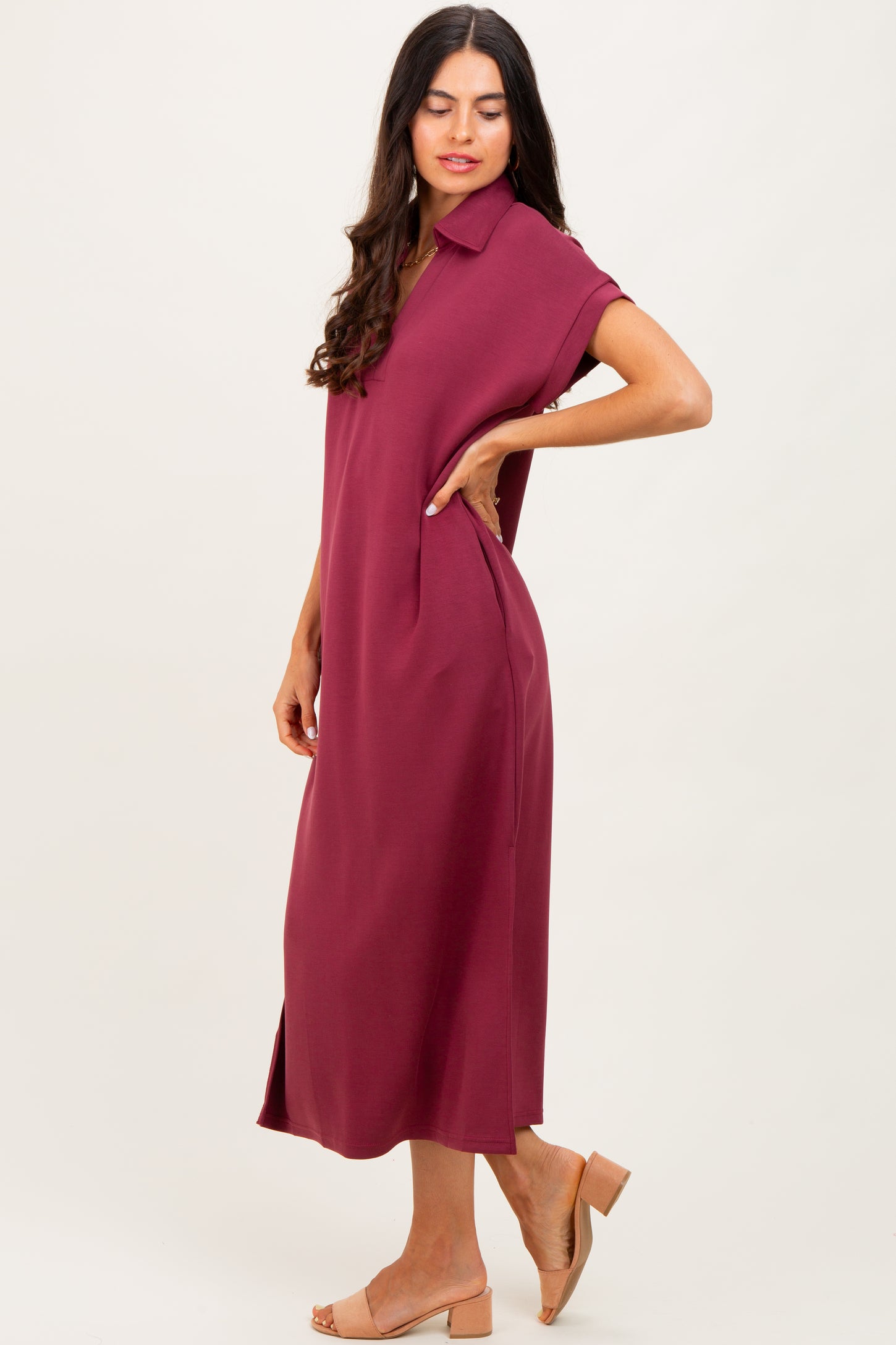 woman wearing a burgundy short sleeve midi dress with a collar and side pockets, standing in profile