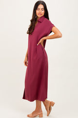woman wearing a burgundy short sleeve midi dress with a collar and side pockets, standing in profile