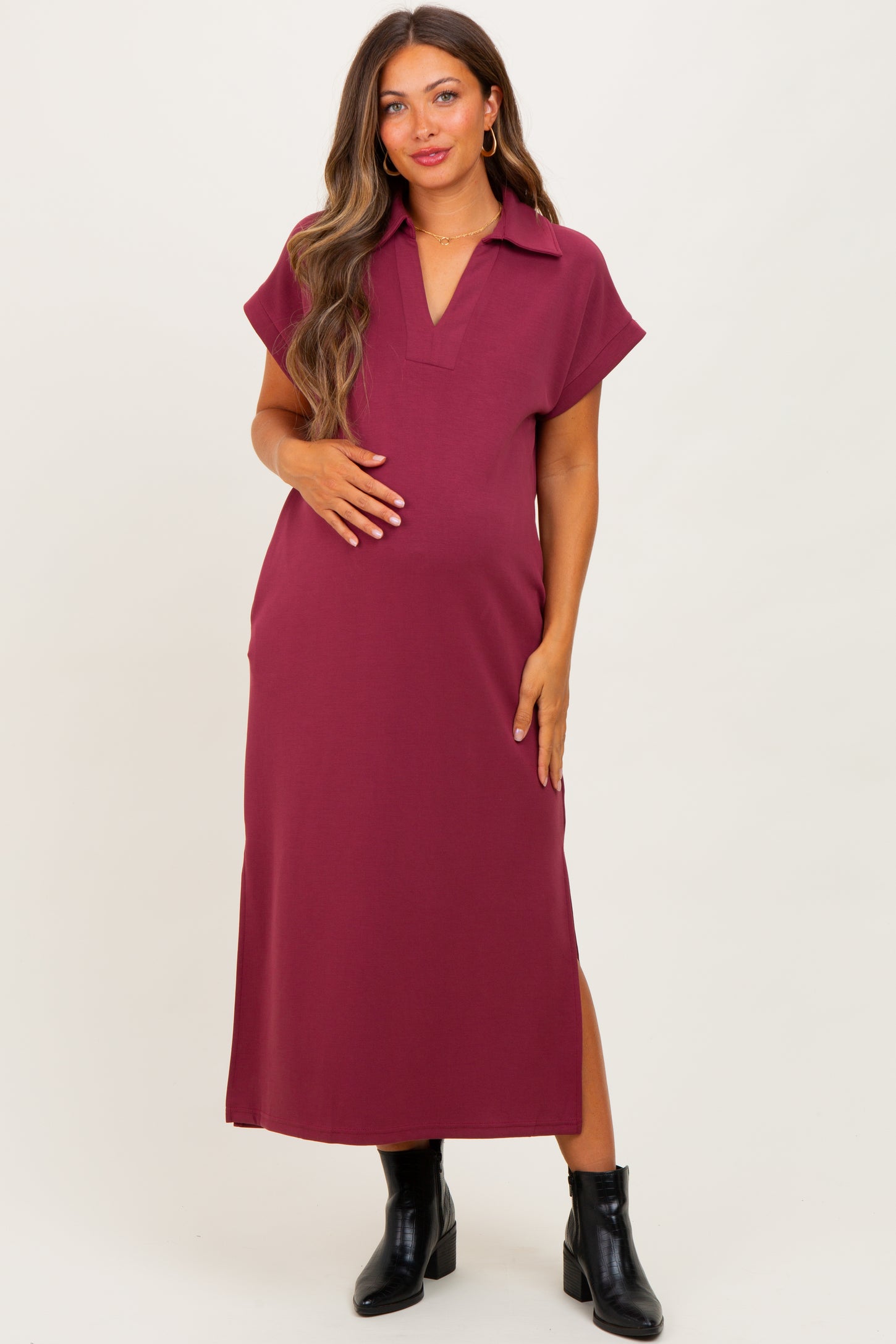 woman wearing a burgundy maternity maxi dress with short sleeves and a collar, holding her baby bump