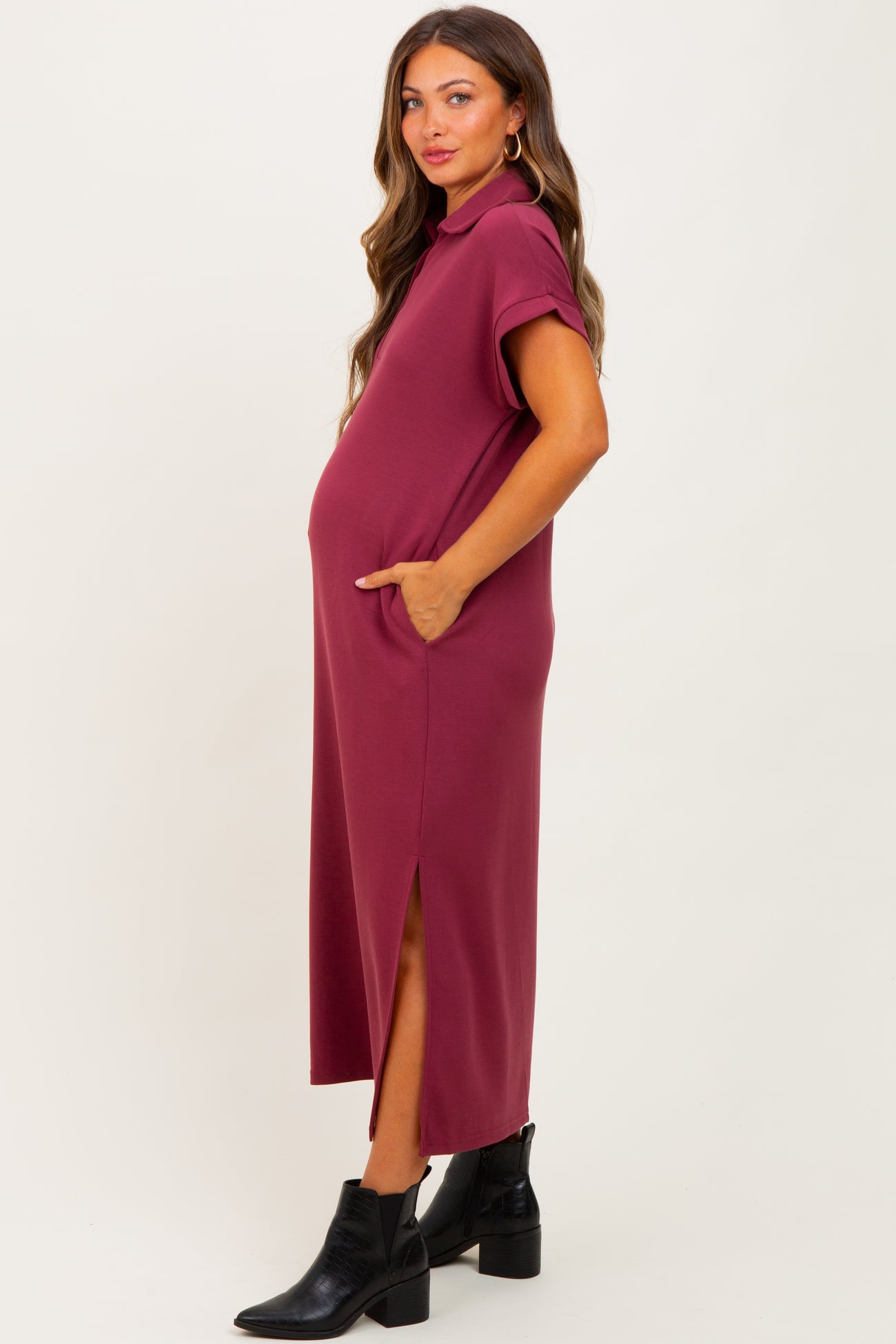 woman wearing a burgundy maternity dress with short sleeves, pockets, and side slits, showing her baby bump