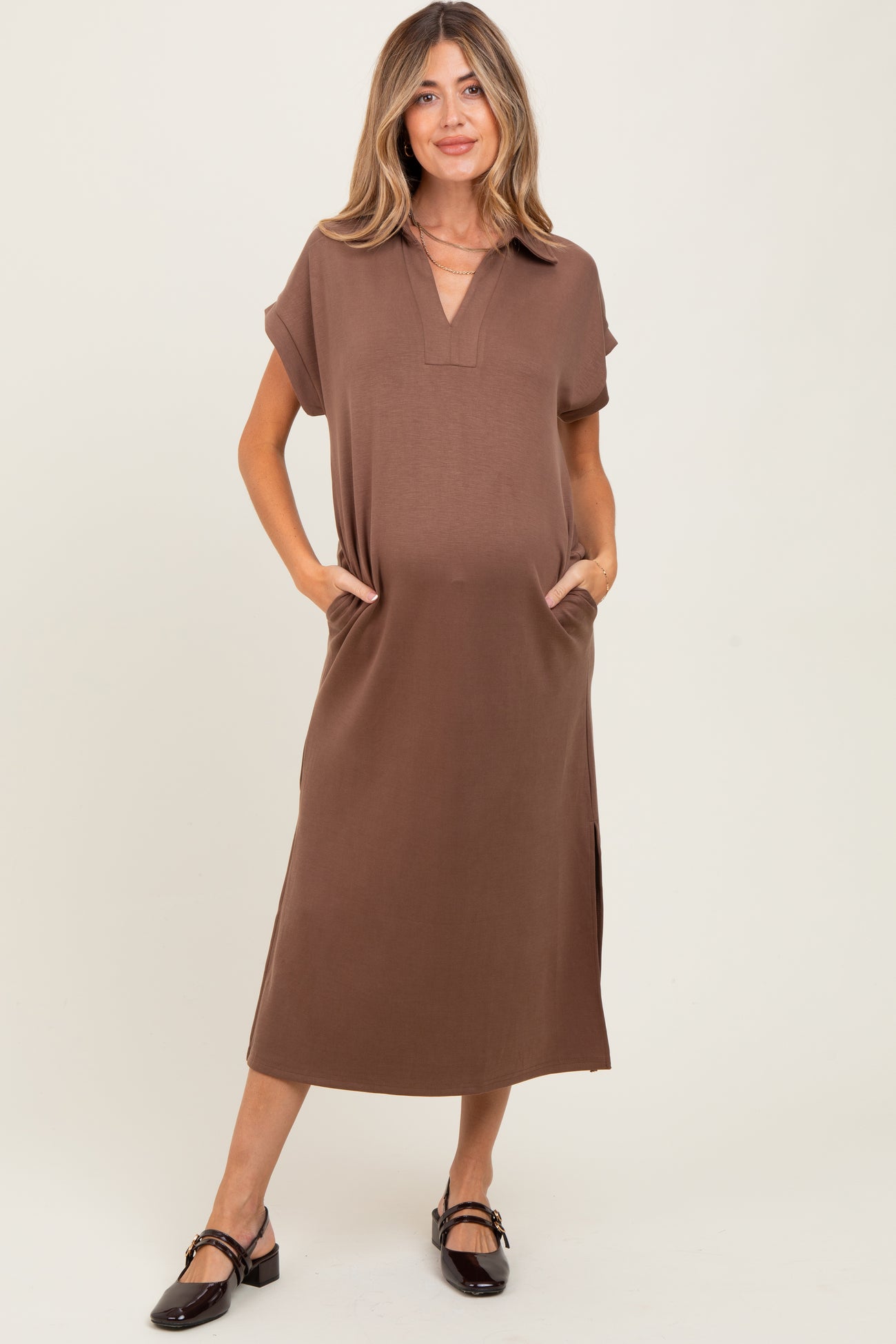 woman wearing a brown short sleeve maternity dress with pockets and side slits, holding her baby bump