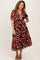 woman wearing a brown floral midi dress with short sleeves and red trim, posing with one hand on her hip