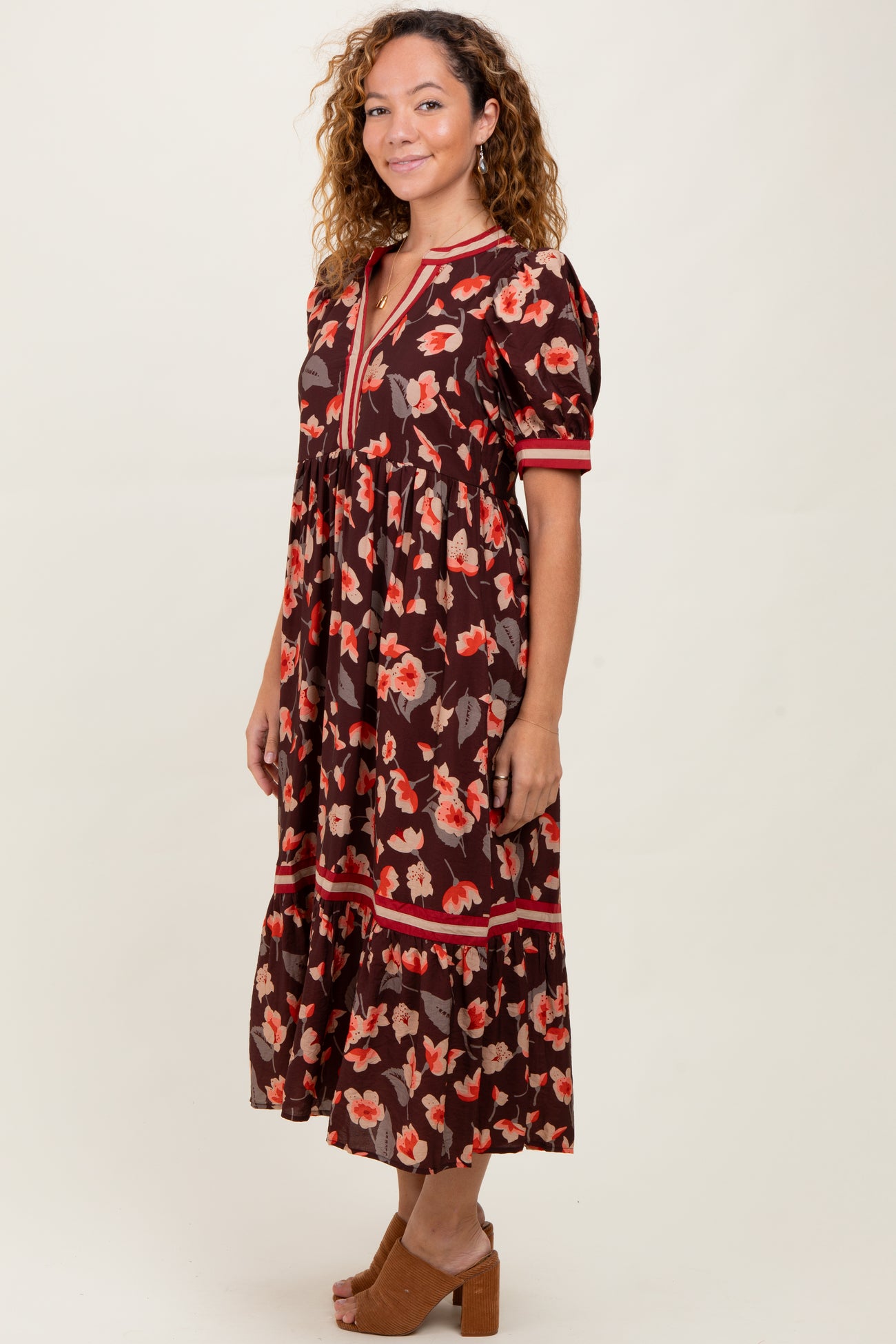 woman wearing a brown floral midi dress with puff sleeves and a v-neckline, standing sideways on a neutral background