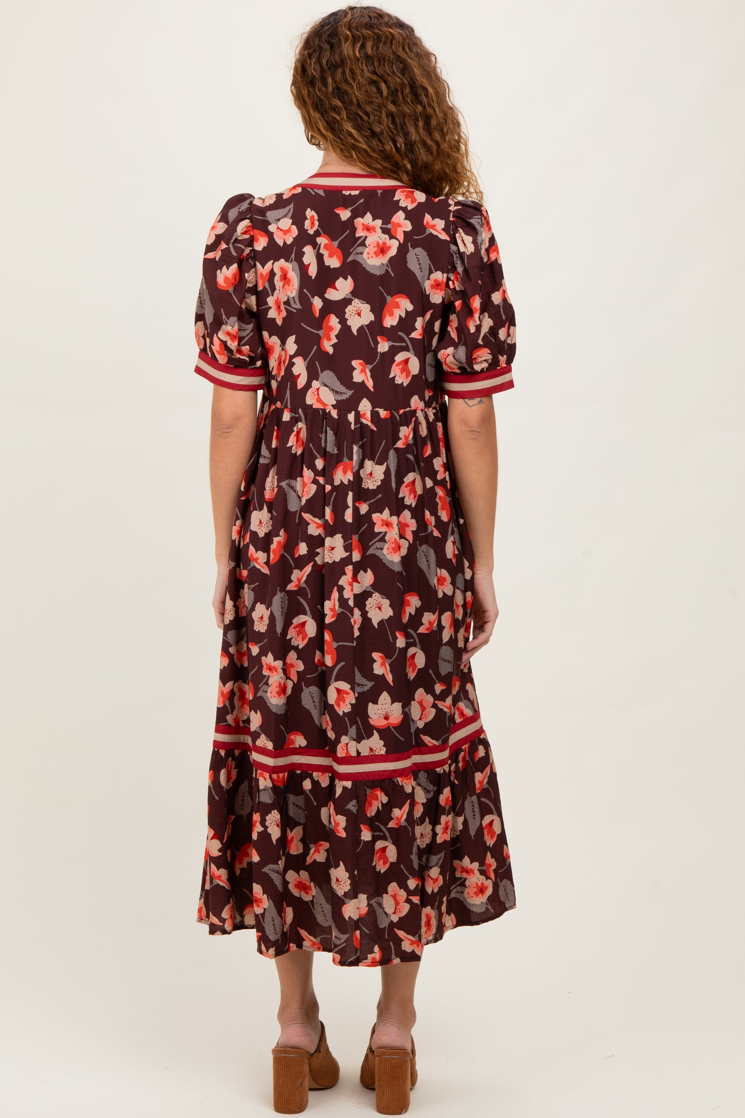 woman wearing a brown floral maxi dress with puff sleeves and red trim, viewed from the back