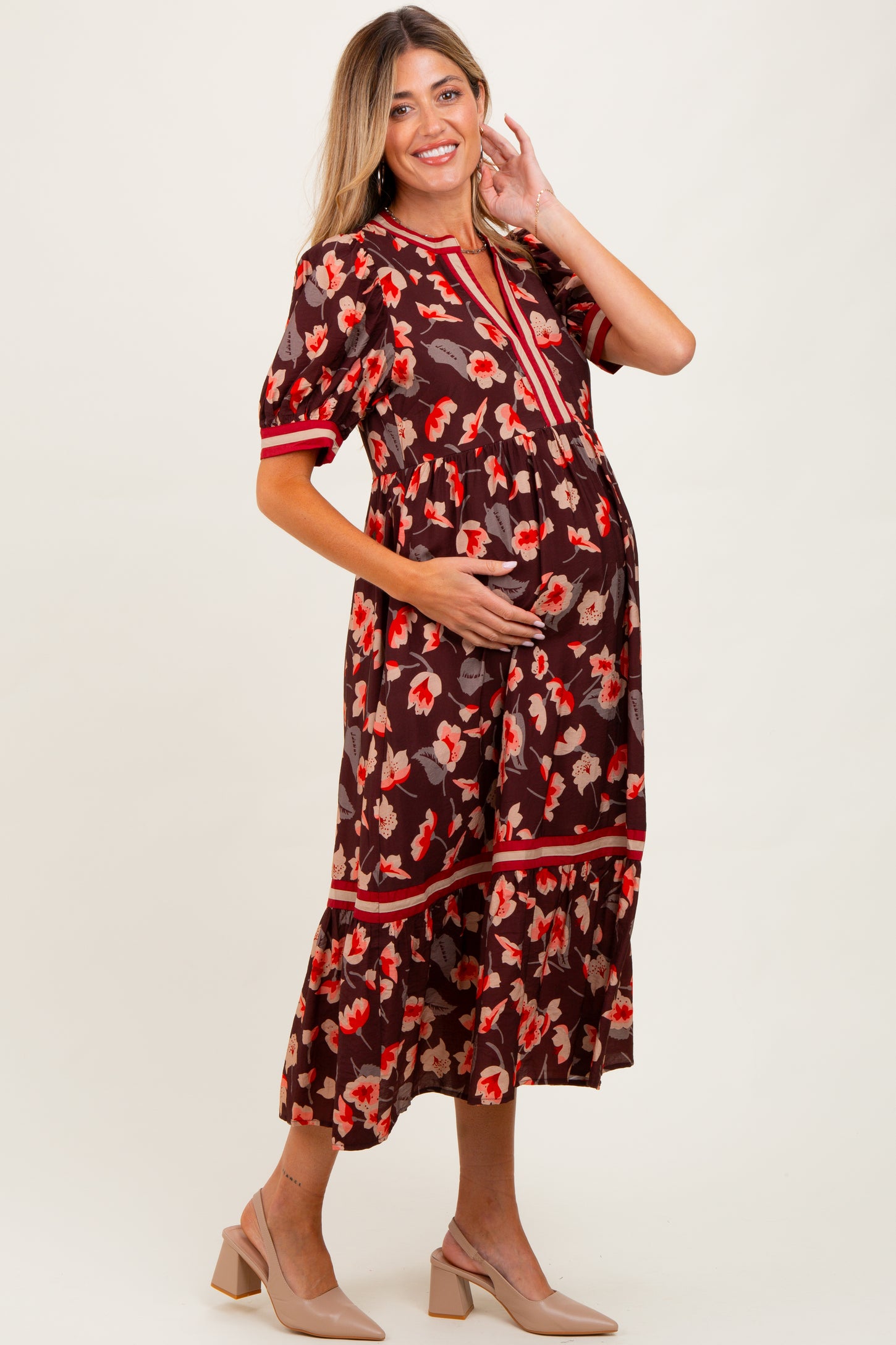 woman wearing a brown floral maternity dress with short sleeves and a tiered skirt, holding her baby bump