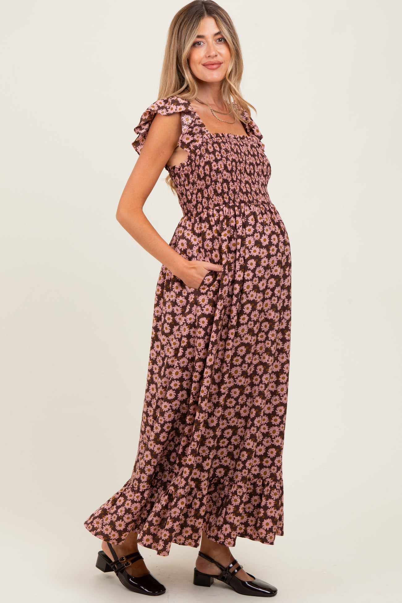 woman wearing a black floral maternity maxi dress with ruffled straps and pockets, displaying her baby bump