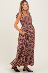 woman wearing a black floral maternity maxi dress with ruffled straps and pockets, displaying her baby bump