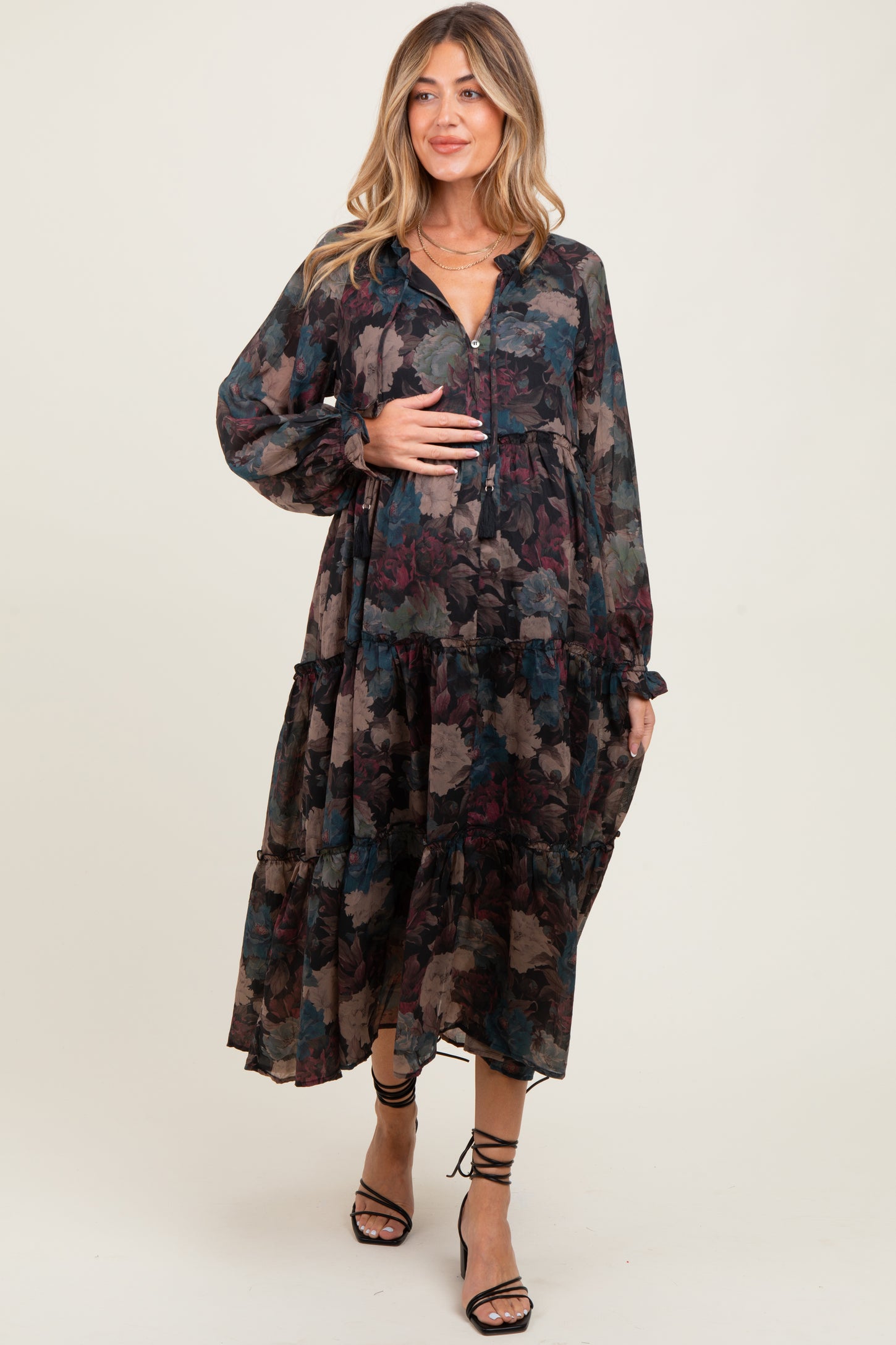 woman wearing a floral print long sleeve maternity dress with a tiered design and holding her baby bump