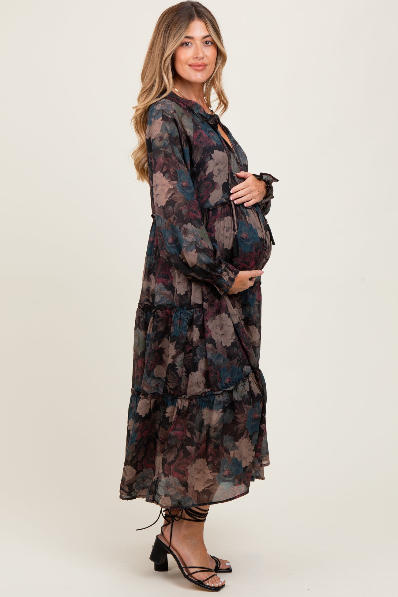 woman wearing a long sleeve black floral maternity dress with a tiered skirt, showing her baby bump