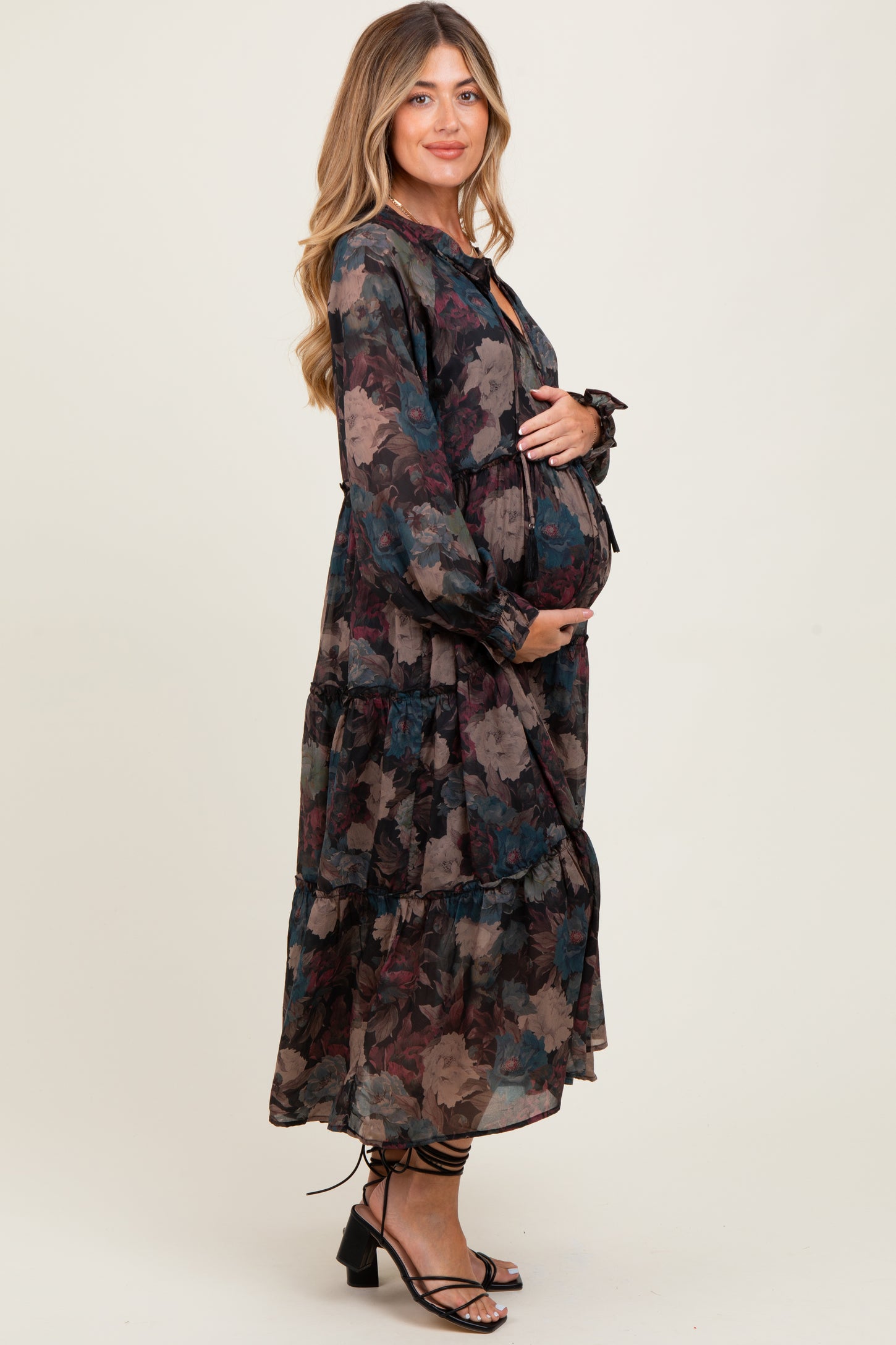woman wearing a long sleeve black floral maternity dress with a tiered skirt, showing her baby bump