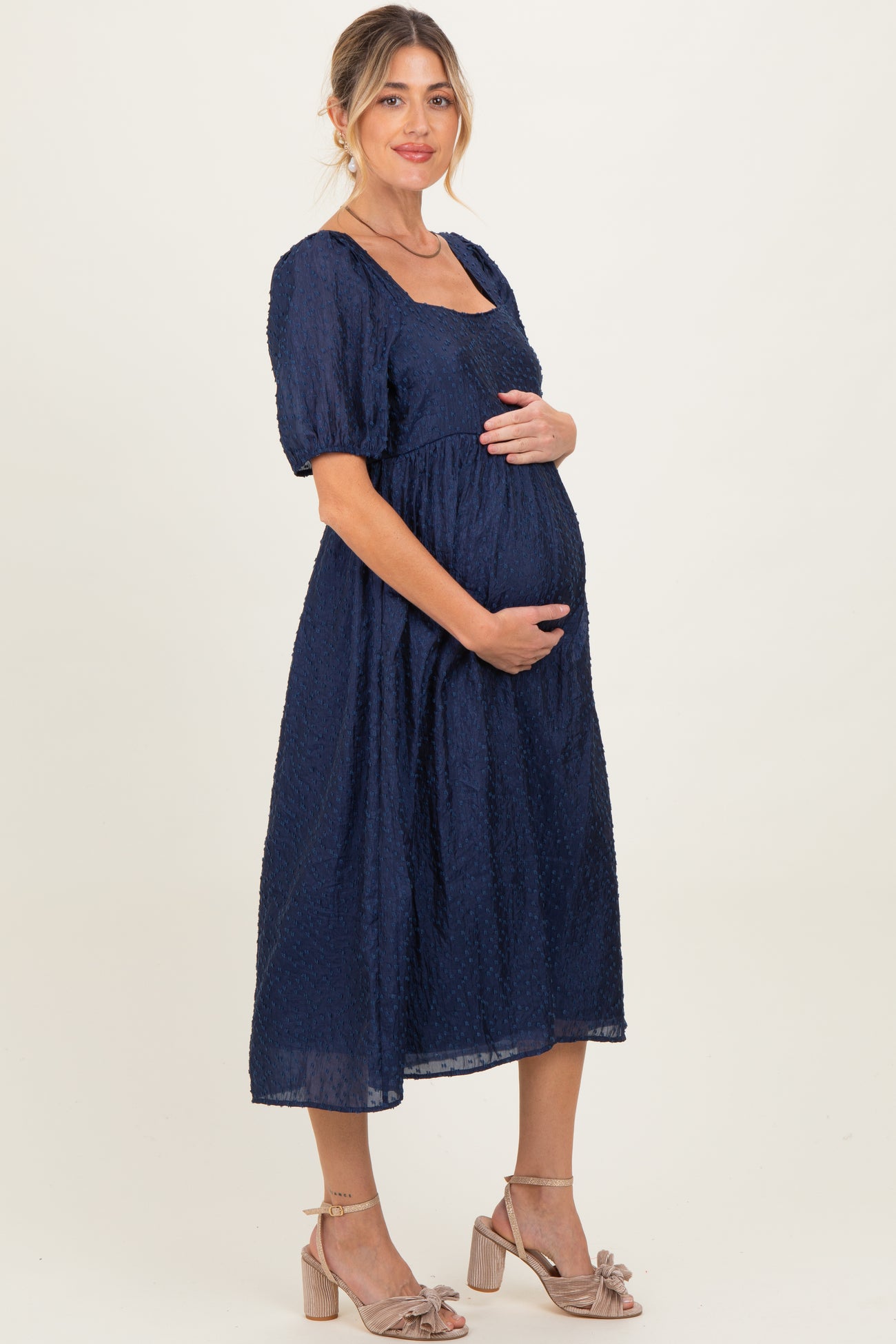 woman wearing a navy blue maternity dress with short puff sleeves and holding her baby bump
