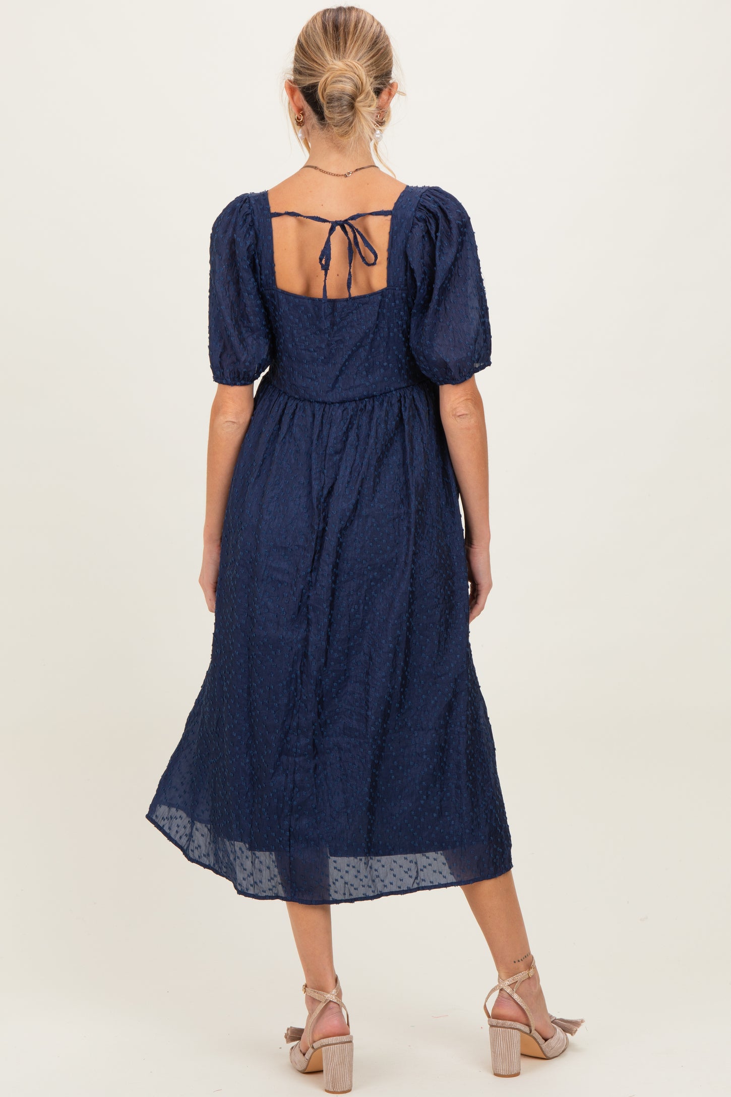 woman wearing a navy blue maternity midi dress with puff sleeves and a tie-back detail