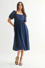 woman wearing a navy blue midi dress with puff sleeves and a square neckline, styled with black heels