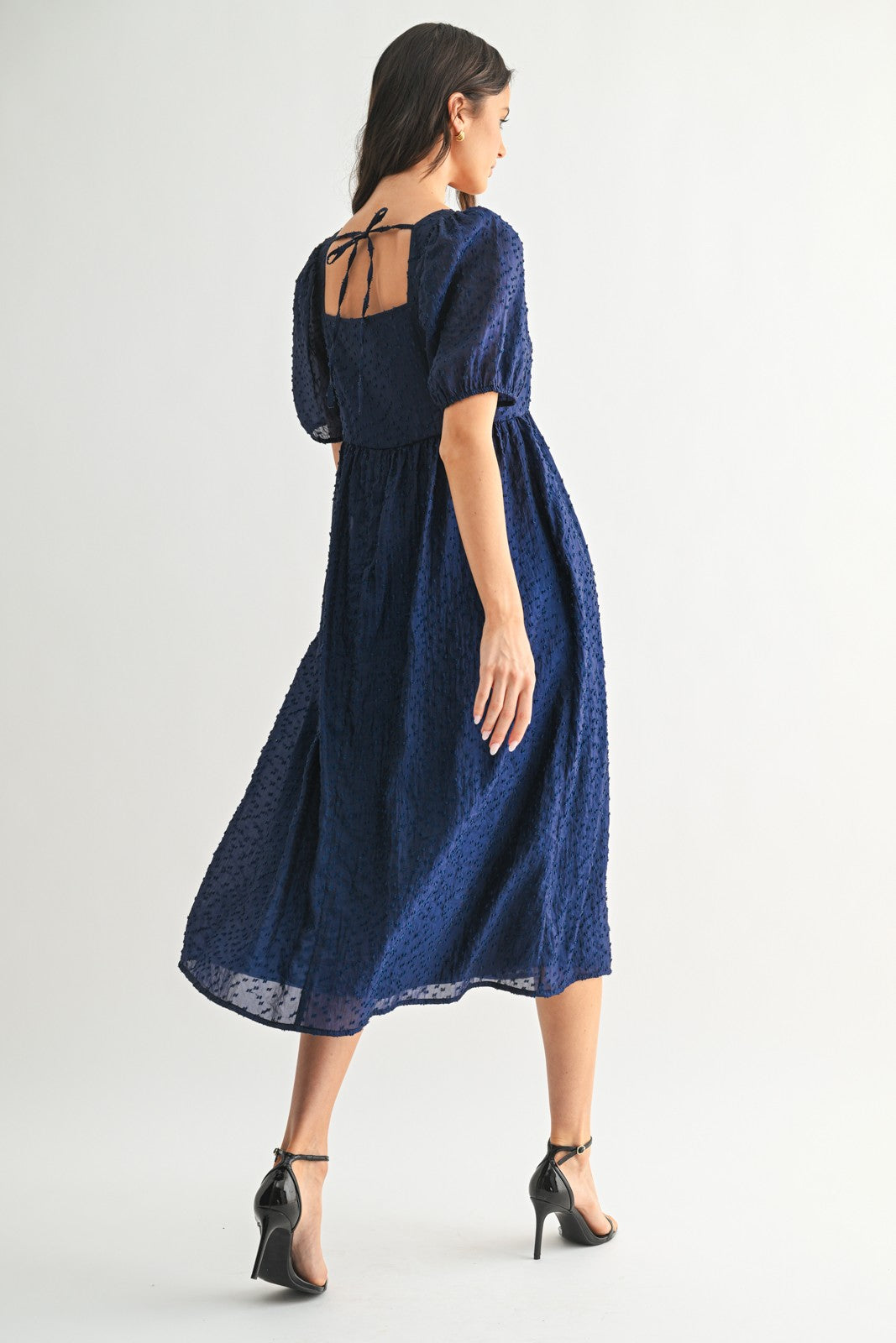 woman wearing a navy blue midi dress with puff sleeves and a tie-back detail, styled with strappy high heels